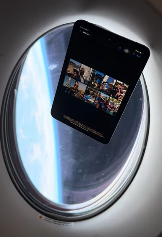 A tablet floating beside a spacecraft window during the Polaris Dawn mission, with Earth's horizon outside. The screen shows a grid of small photos sent to space through the My Face in Space program.